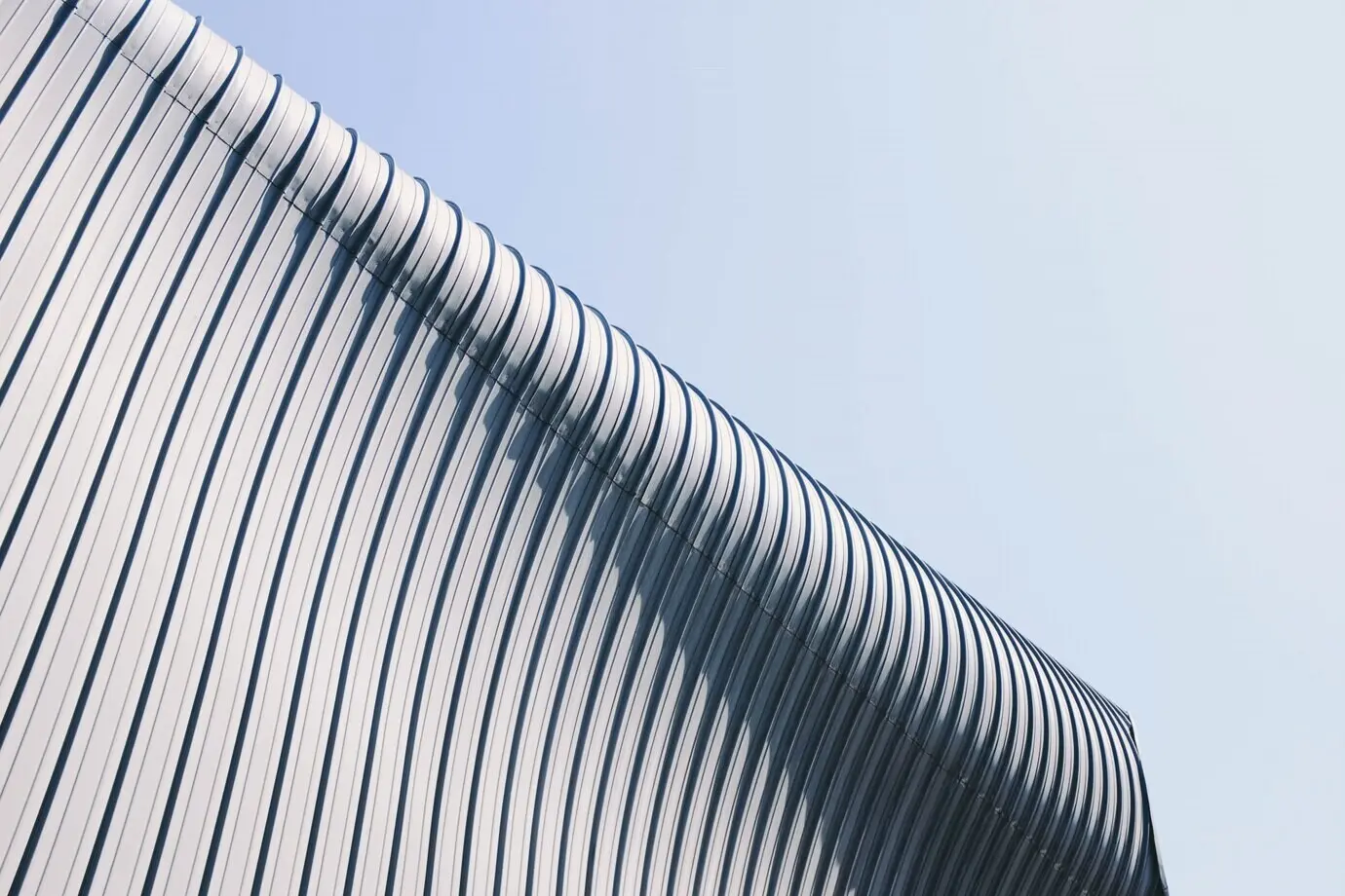 Tiefwinkelaufnahme eines grau-weißen Gebäudedachs mit interessanten Texturen unter blauem Himmel.